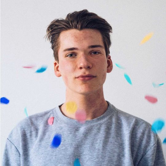 A male standing and looking straight ahead while confetti falls over him