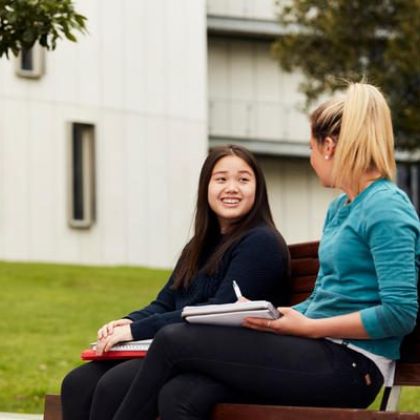 Two students sitting on a bench outside and chatting