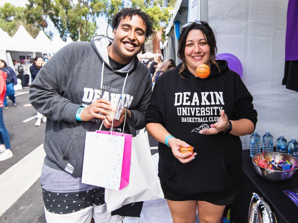 Two students wearing DUSA hoodie and TShirt standing in front of a stand at the DUSA Clubs event