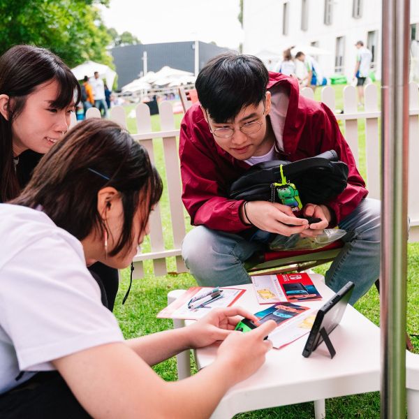 Group of students sitting outside looking inquisitively at an ipad screen