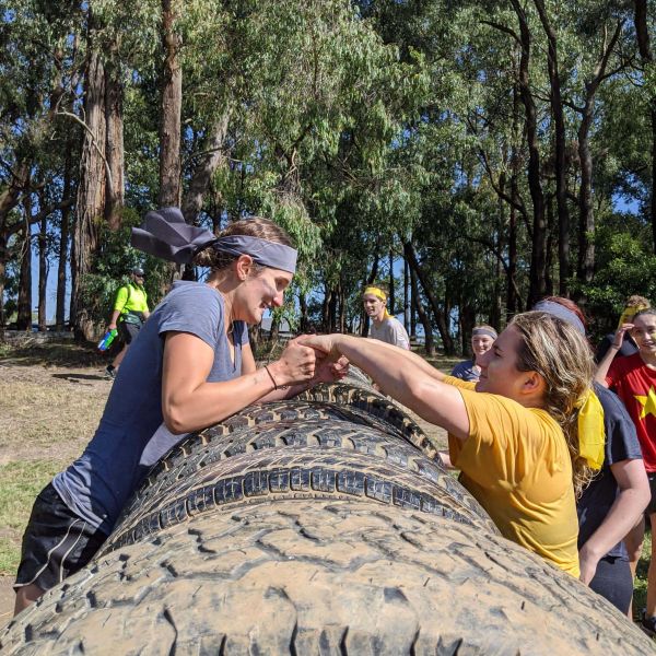 Two students gripping hands over a large tire during a DUSA activity