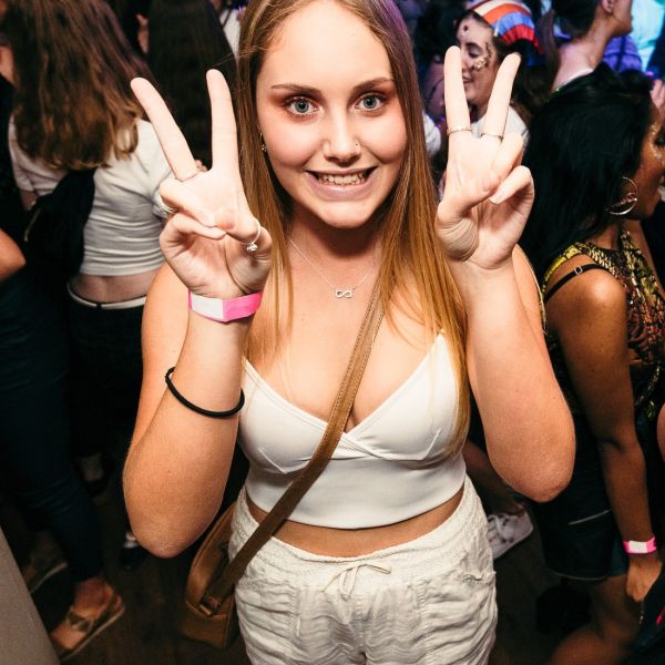 Female student at a DUSA event holding both hands up and demonstrating the peace sign
