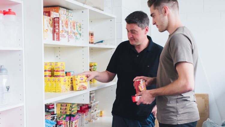 Male student and Advocacy staff member standing in front of shelves of food at the DUSA Survival Centre