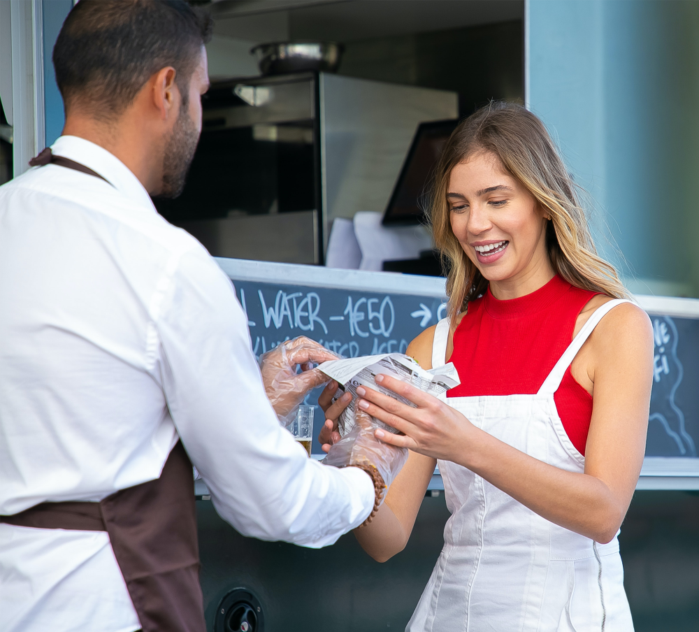 A man serving food to a female at the front of his food truck