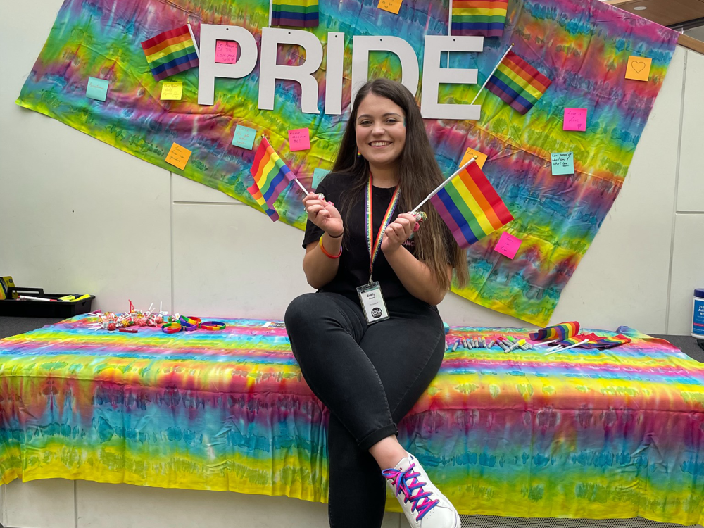 Student Council President Emily sitting on a table covered in bright colours and holding the pride flag
