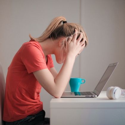 Female student sitting at a desk looking at her laptop with her head in her hands