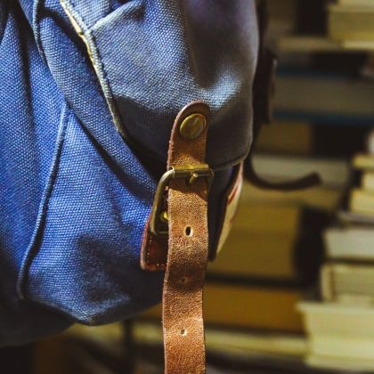 A denim backpack with book sitting on a shelf in the background