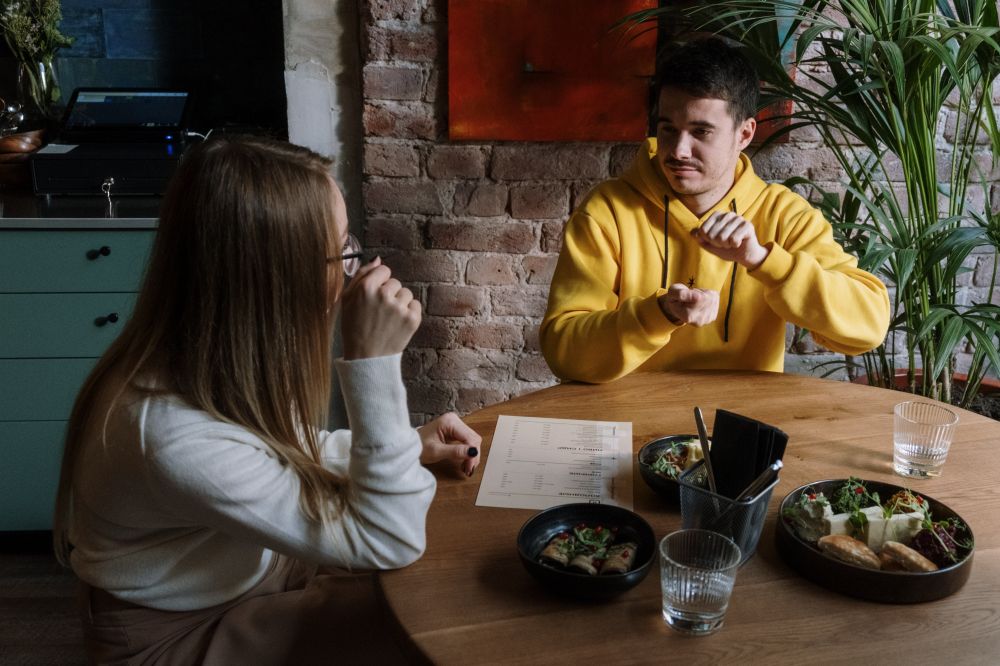Male signing to a female while sitting around a table