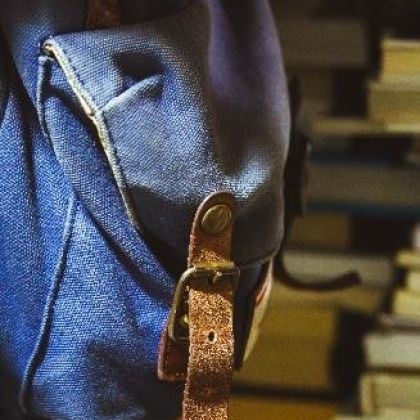 A denim back pack with books on shelves in the background