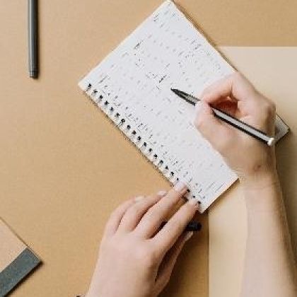 a notebook on a desk with a person using a pen to write notes
