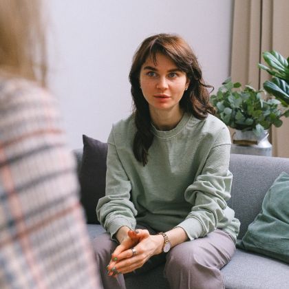 young woman in a green jumper sitting on a grey couch with a green cushion next to her in a counselling session