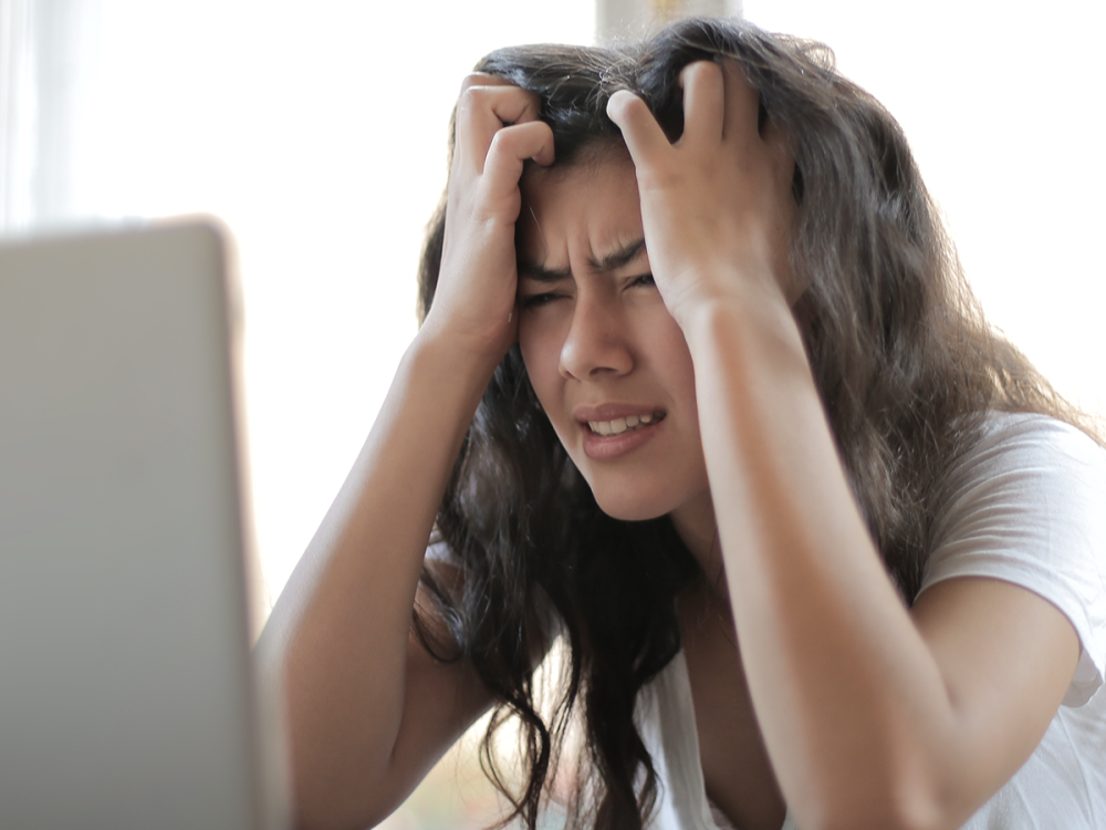 A stressed young woman sitting in front of a laptop with her hands in her face