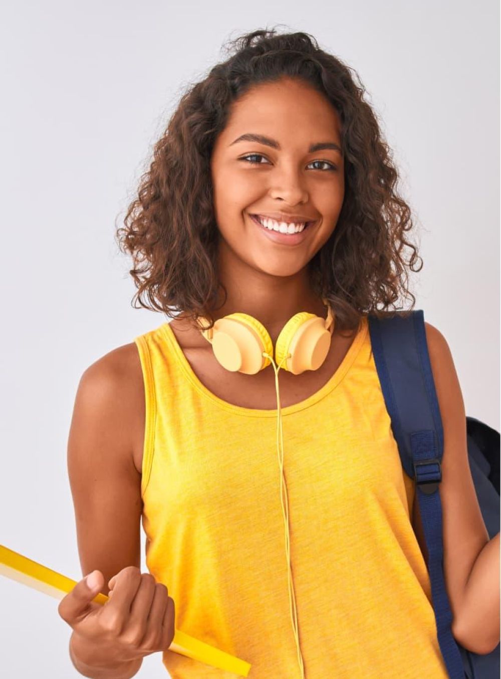 Female carrying a backpack and smiling with yellow headphones around her neck