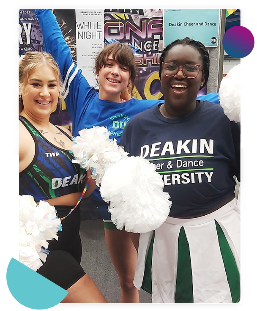 Three girls of the Deakin Cheers Club holding up their pom poms and smiling