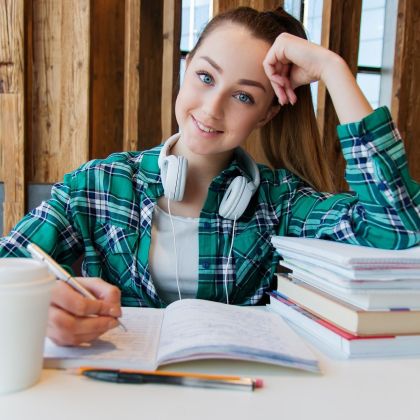 Female student smiling and sitting at a desk full of textbooks and a take away coffee